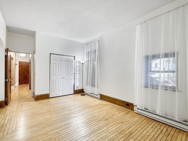 unfurnished bedroom featuring light wood-type flooring, a textured ceiling, a closet, and a baseboard radiator