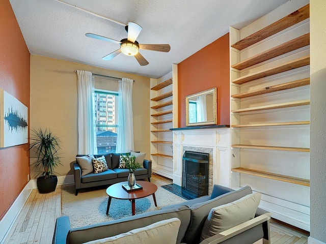 living room with built in shelves, a ceiling fan, a textured ceiling, wood finished floors, and baseboards