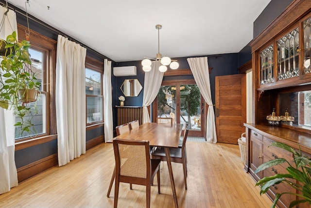 dining space with a chandelier, a healthy amount of sunlight, a wall mounted AC, and light hardwood / wood-style floors