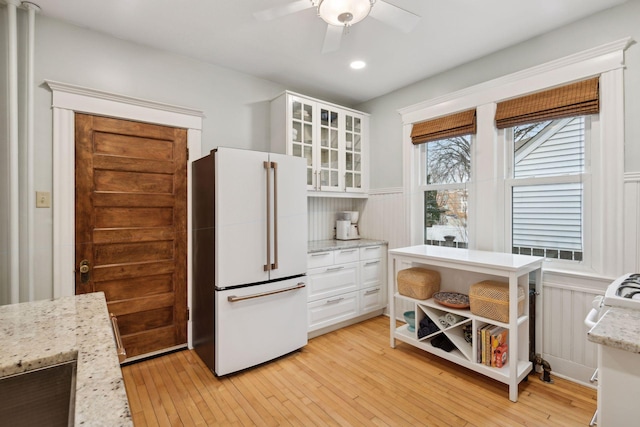 kitchen with white cabinets, ceiling fan, light stone counters, high end fridge, and light hardwood / wood-style flooring