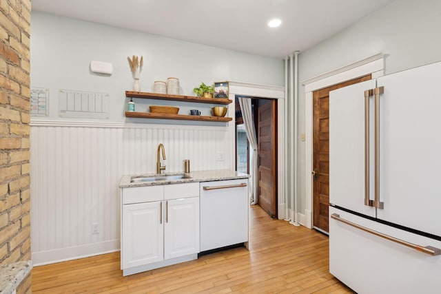 kitchen with white cabinetry, sink, light wood-type flooring, light stone counters, and white appliances