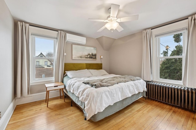 bedroom with radiator heating unit, light hardwood / wood-style floors, an AC wall unit, and ceiling fan