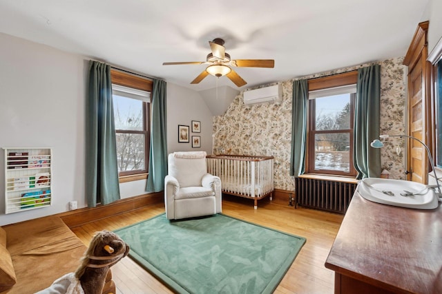 living area featuring an AC wall unit, radiator, light wood-type flooring, and plenty of natural light