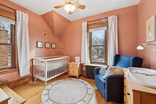 bedroom featuring a nursery area, ceiling fan, radiator, and light hardwood / wood-style flooring