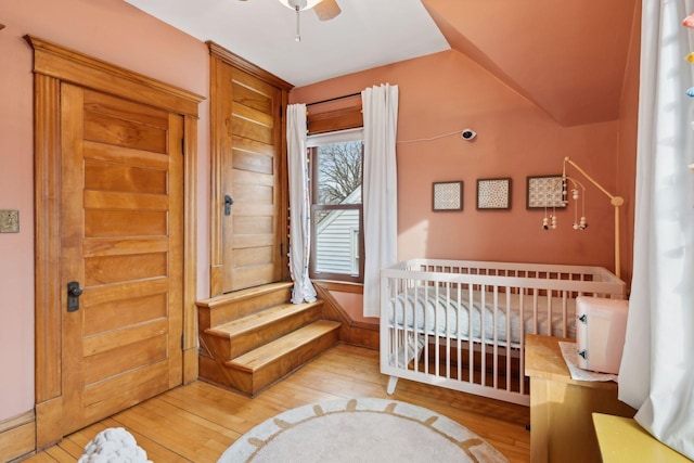 bedroom featuring lofted ceiling, a nursery area, ceiling fan, and light wood-type flooring