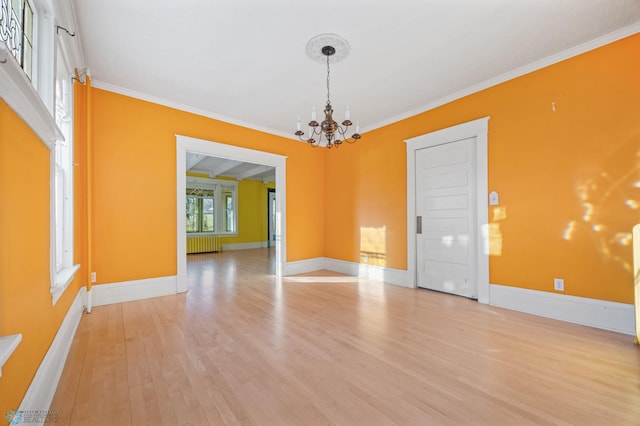 empty room with crown molding, radiator, light wood-style flooring, a chandelier, and baseboards