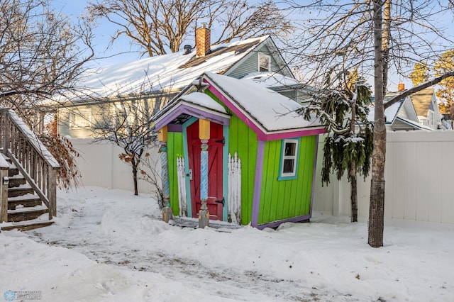 snow covered structure with a garage, an outbuilding, and fence