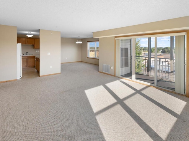 unfurnished living room with sink, light carpet, and a notable chandelier