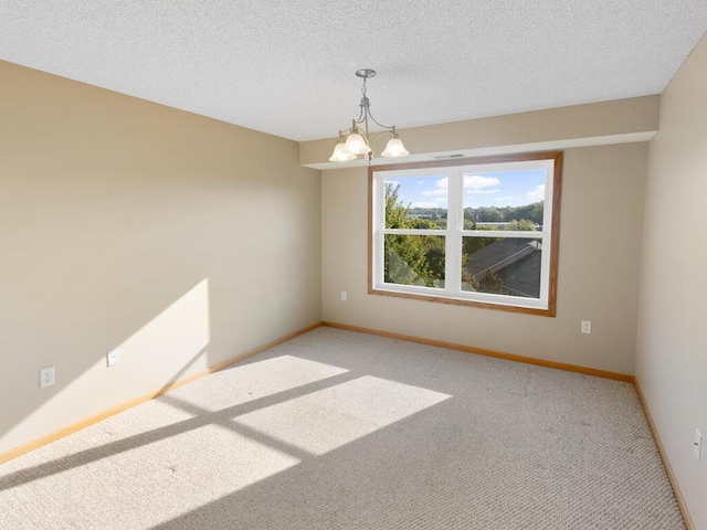 spare room featuring an inviting chandelier, carpet floors, and a textured ceiling