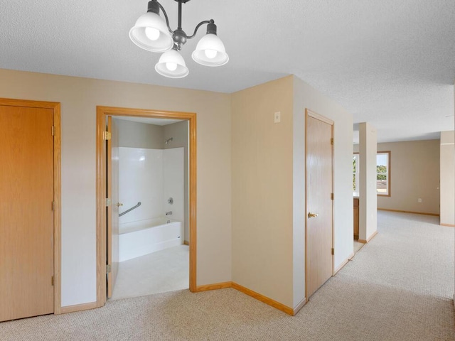 hallway with light colored carpet, a textured ceiling, and an inviting chandelier