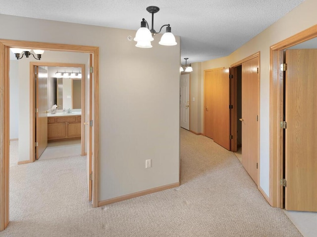 hallway featuring a textured ceiling, an inviting chandelier, and light colored carpet