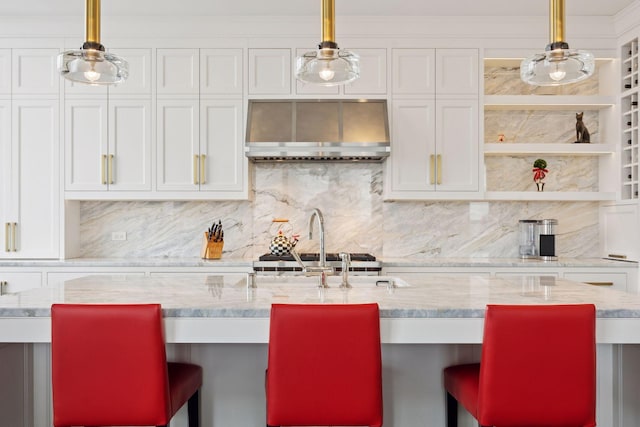 kitchen with a breakfast bar, wall chimney range hood, white cabinets, and decorative light fixtures