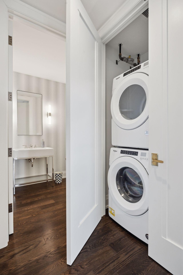 laundry area featuring stacked washer / drying machine and dark hardwood / wood-style flooring