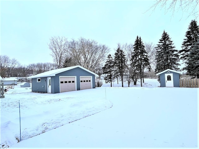 yard layered in snow featuring a garage and a storage shed