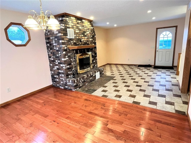 unfurnished living room featuring a chandelier, hardwood / wood-style flooring, a brick fireplace, and plenty of natural light