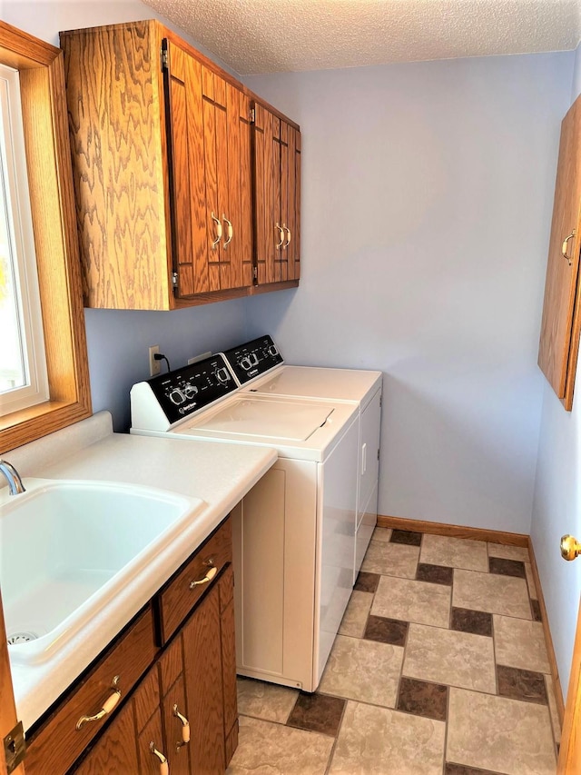 laundry area with washing machine and clothes dryer, sink, cabinets, and a textured ceiling