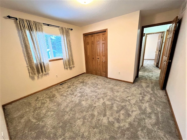unfurnished bedroom with a textured ceiling, carpet, baseboards, visible vents, and a closet