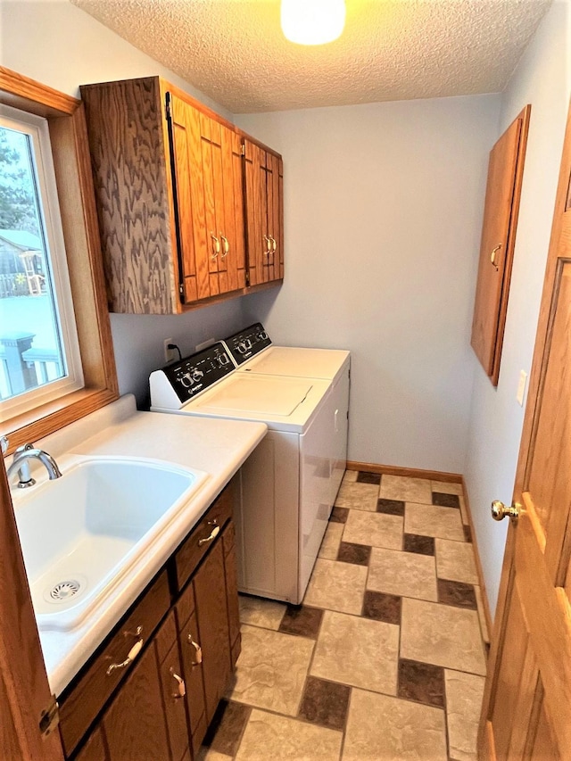 laundry area featuring cabinet space, separate washer and dryer, a textured ceiling, and a sink