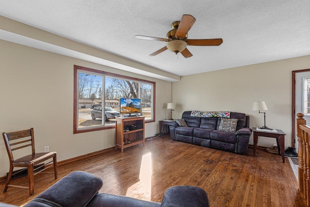 living room with a ceiling fan, a textured ceiling, baseboards, and wood finished floors