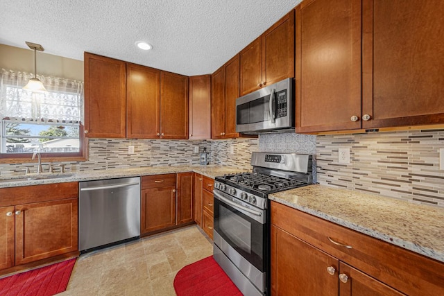 kitchen featuring light stone counters, brown cabinets, backsplash, appliances with stainless steel finishes, and a sink