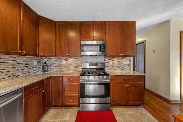 kitchen with light stone counters, stainless steel appliances, backsplash, a textured ceiling, and baseboards