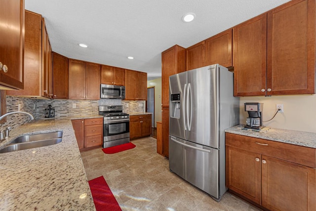 kitchen featuring a sink, light stone countertops, stainless steel appliances, backsplash, and recessed lighting