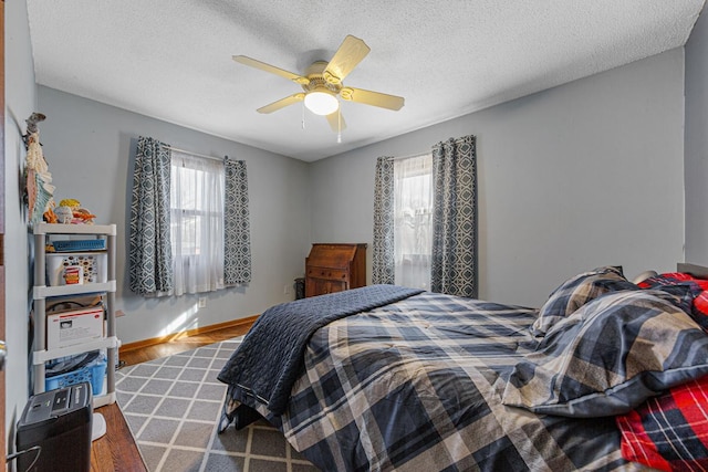 bedroom with a textured ceiling, multiple windows, baseboards, and wood finished floors