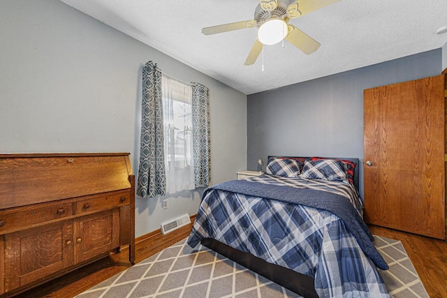 bedroom with ceiling fan, wood finished floors, visible vents, and baseboards