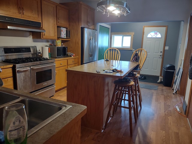 kitchen with light hardwood / wood-style floors, a kitchen island, sink, a breakfast bar area, and stainless steel appliances