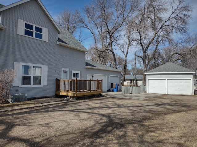 view of side of property featuring central air condition unit, a shingled roof, a wooden deck, and an outbuilding