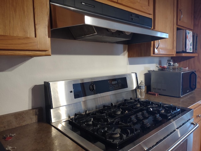 details featuring gas range oven, under cabinet range hood, dark countertops, black microwave, and brown cabinets