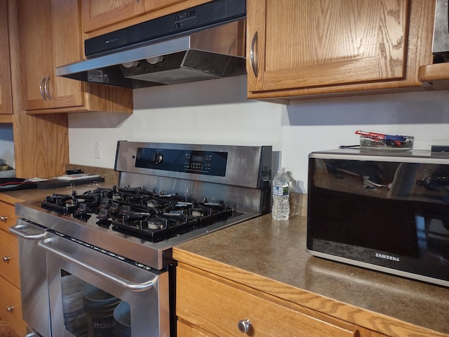 kitchen featuring under cabinet range hood, stainless steel gas range oven, and dark countertops