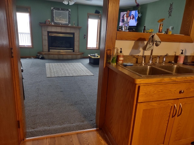 bar featuring carpet flooring, a sink, a tiled fireplace, a ceiling fan, and indoor wet bar