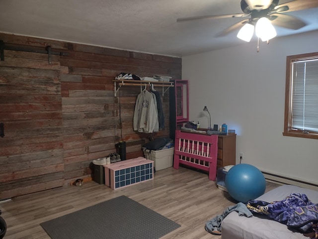 exercise area with a baseboard radiator, a ceiling fan, wood walls, and wood finished floors