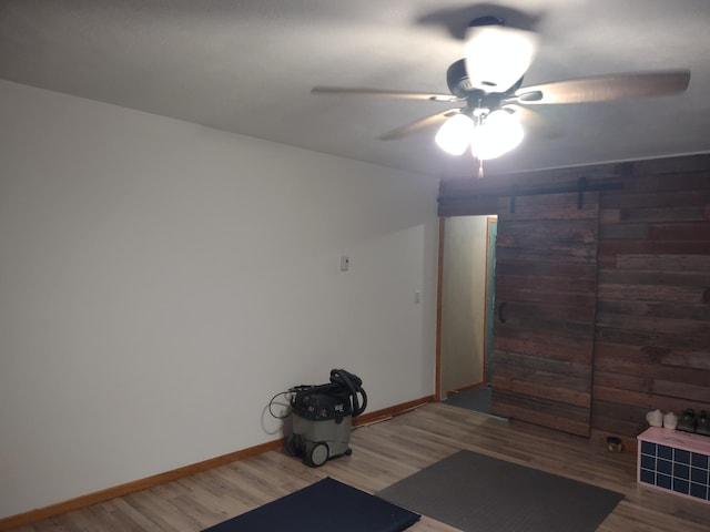 interior space featuring baseboards, a barn door, wood finished floors, and a ceiling fan