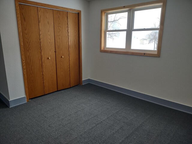 unfurnished bedroom with a closet, baseboards, and dark colored carpet