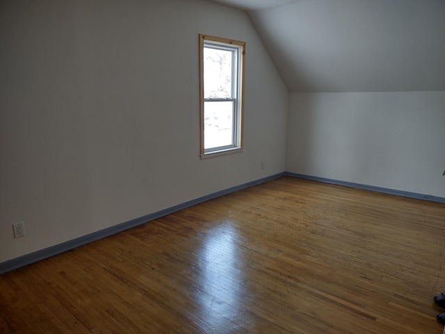 additional living space with hardwood / wood-style floors, baseboards, and vaulted ceiling