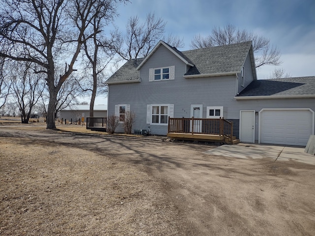 rear view of house with driveway, a shingled roof, a deck, and an attached garage