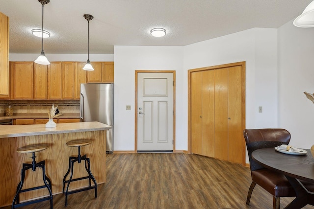 kitchen featuring backsplash, a textured ceiling, pendant lighting, stainless steel refrigerator, and a breakfast bar area