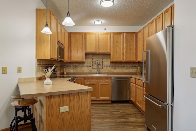 kitchen with kitchen peninsula, pendant lighting, a textured ceiling, a breakfast bar, and appliances with stainless steel finishes