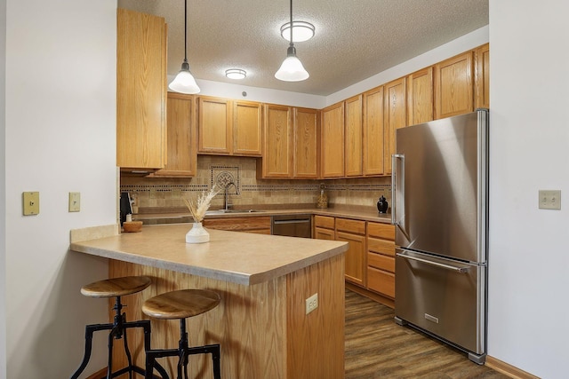 kitchen featuring backsplash, a textured ceiling, appliances with stainless steel finishes, decorative light fixtures, and kitchen peninsula