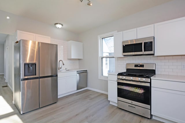 kitchen with sink, white cabinets, light hardwood / wood-style flooring, backsplash, and appliances with stainless steel finishes