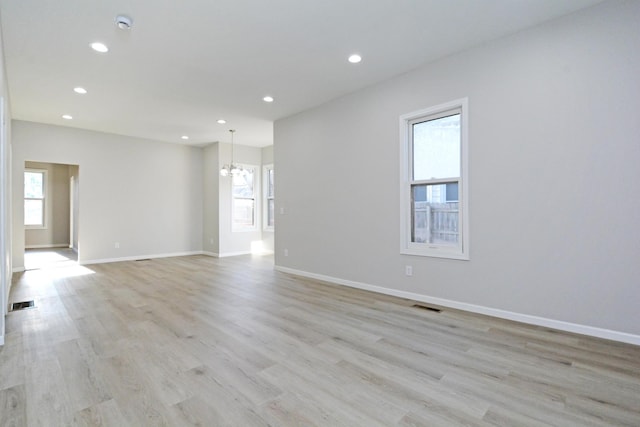 spare room with light wood-type flooring, a chandelier, and a wealth of natural light