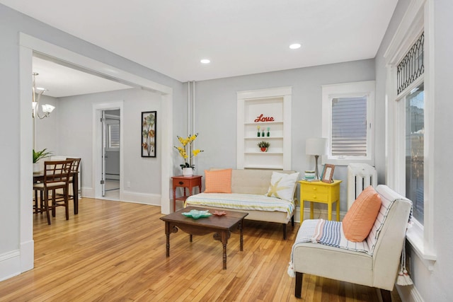 living room with an inviting chandelier, light hardwood / wood-style floors, built in features, and radiator heating unit