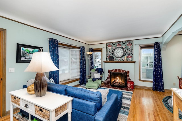 living room with a brick fireplace, plenty of natural light, crown molding, and light hardwood / wood-style floors