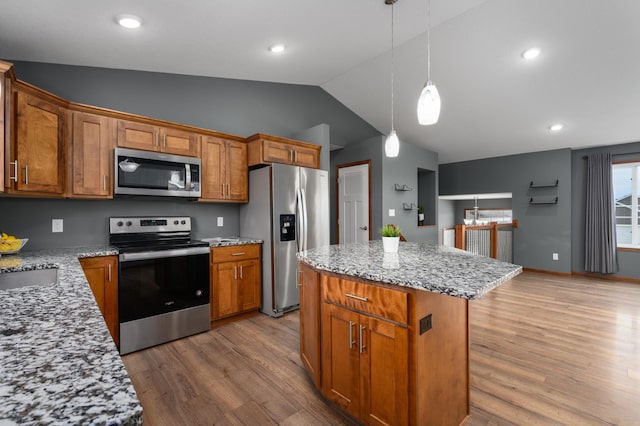 kitchen featuring brown cabinetry, light wood-style flooring, appliances with stainless steel finishes, a center island, and hanging light fixtures