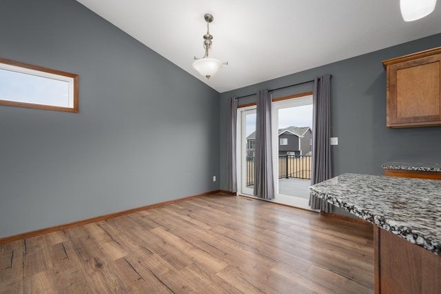 unfurnished dining area with baseboards, vaulted ceiling, and wood finished floors