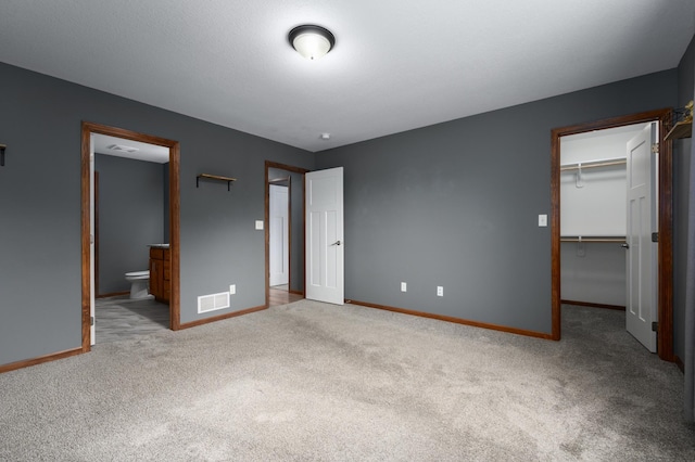 unfurnished bedroom with light carpet, baseboards, visible vents, a walk in closet, and a closet