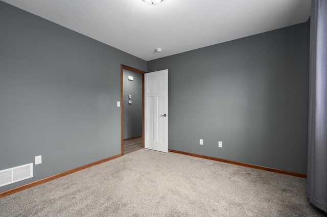 spare room featuring a textured ceiling, carpet floors, visible vents, and baseboards