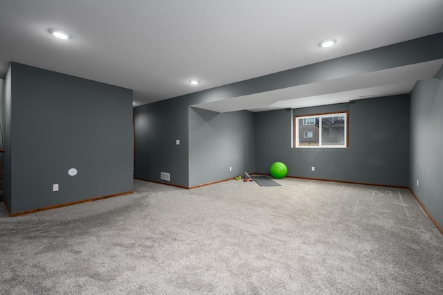 basement featuring a textured ceiling, carpet floors, visible vents, and baseboards